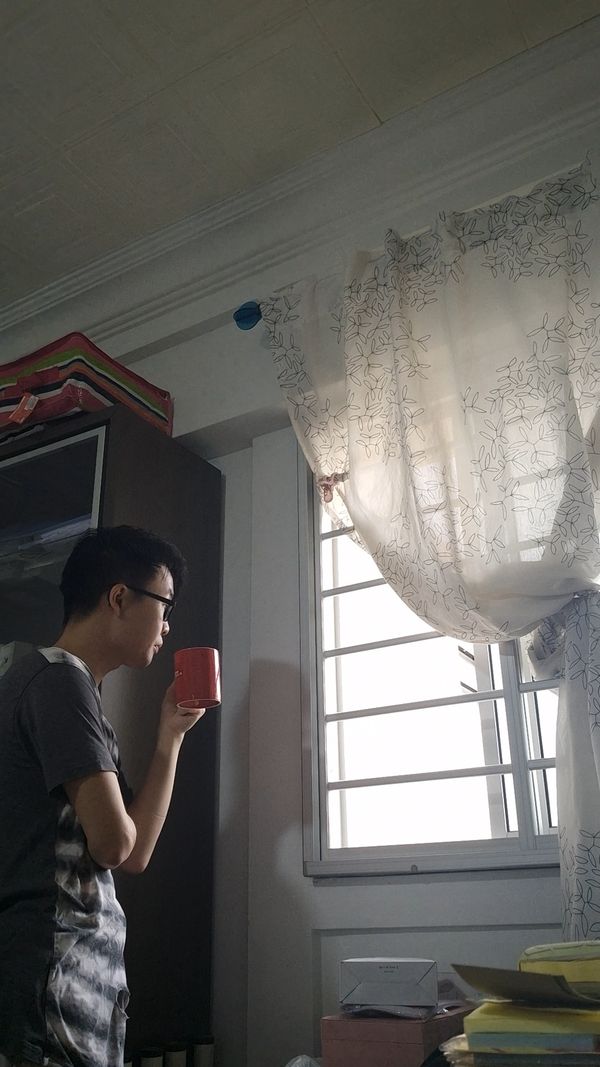 Chuan Long by a window at home, drinking from a red mug